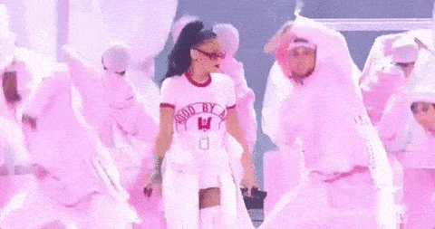 Rihanna dancing on stage with a pink outfit with an ensemble of background dancers behind her wearing outfits with the same shade of pink.